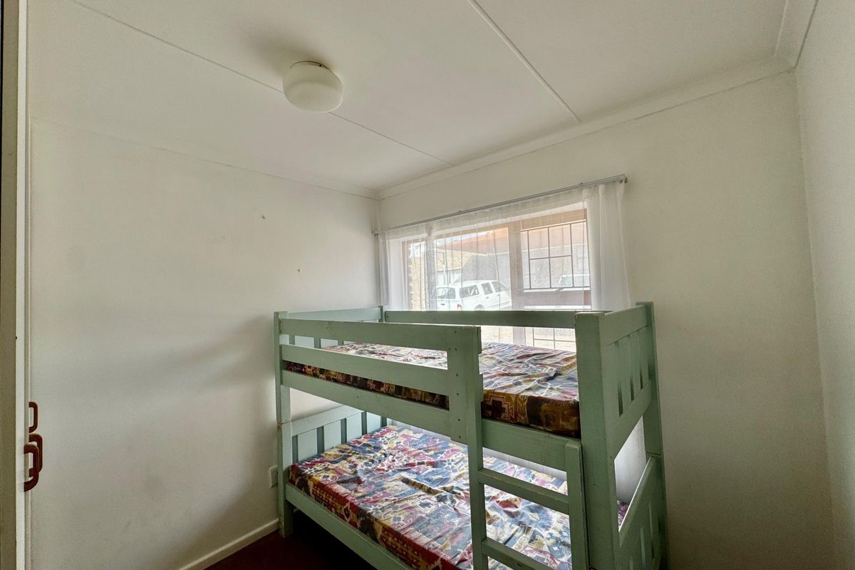 A compact bedroom featuring a window with security bars and a simple ceiling light fixture.