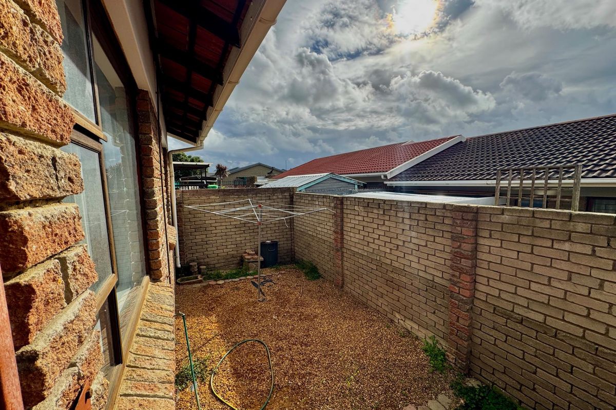 A private rear courtyard area featuring brick boundary walls, gravel ground cover, and a covered roof overhang.