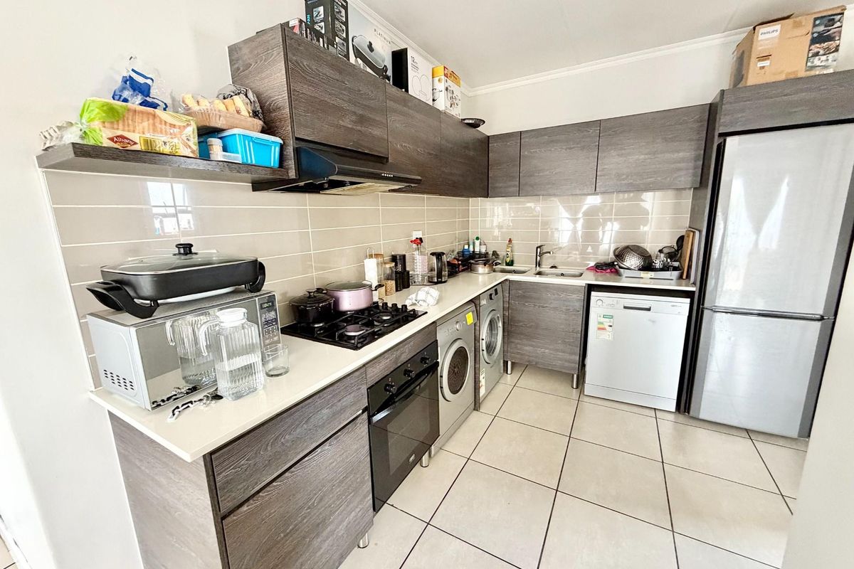 Modern kitchen featuring dark wood-grain cabinetry, gas hob, under-counter oven, extractor fan, and tiled flooring with integrated appliance spaces.