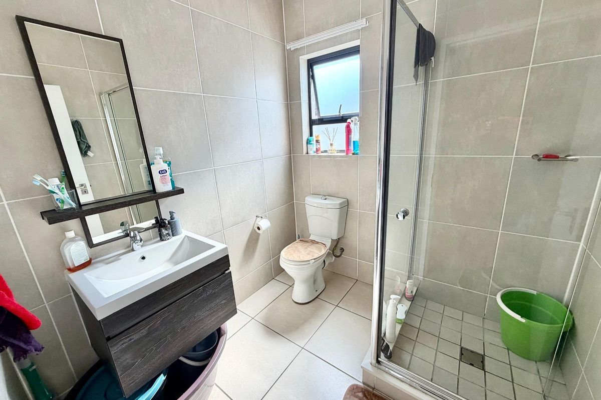 A functional bathroom featuring a modern vanity cabinet, a glass-enclosed shower, and neutral floor-to-ceiling tiling throughout.