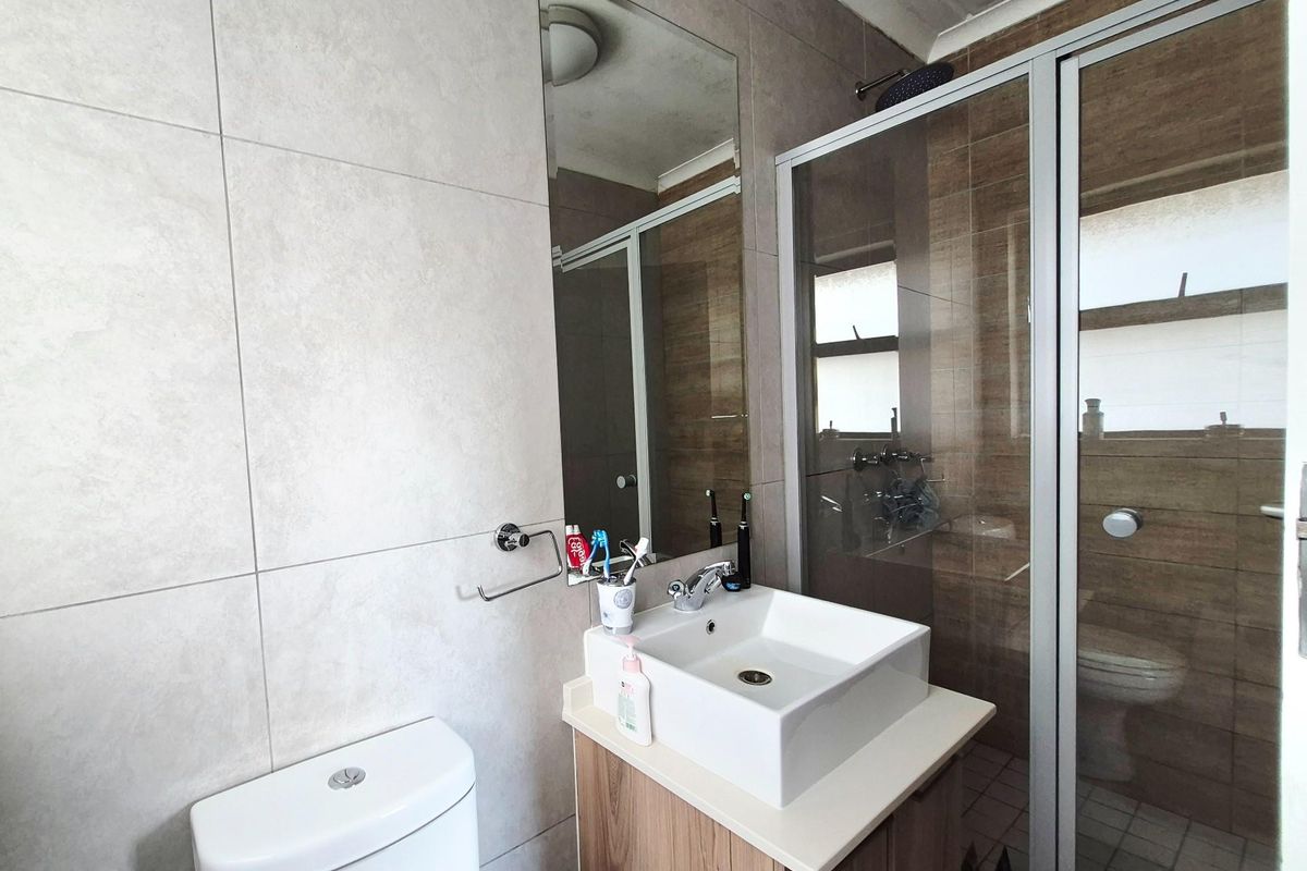 A compact bathroom featuring a modern vessel sink vanity, a glass-enclosed shower, and a wall-mounted toilet with neutral wall tiling.
