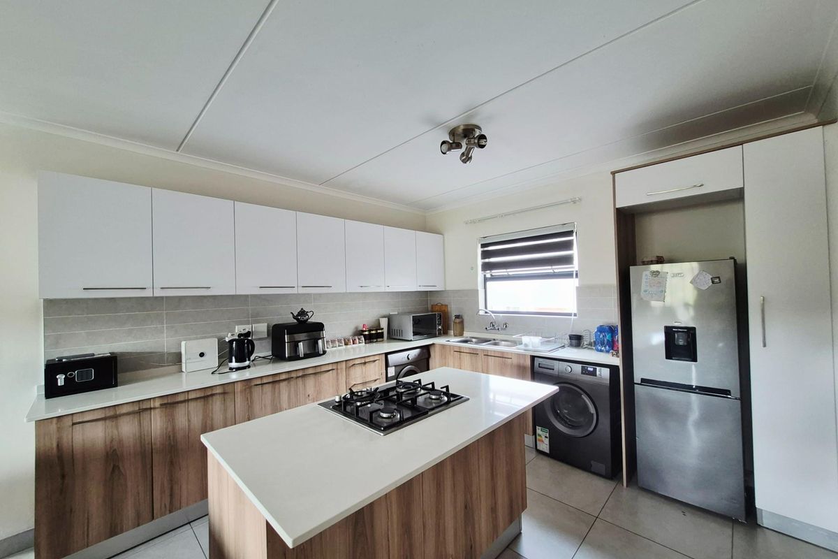 Modern kitchen featuring a central island with a built-in gas hob, sleek wood-grain cabinetry, stone countertops, and integrated space for laundry appliances.