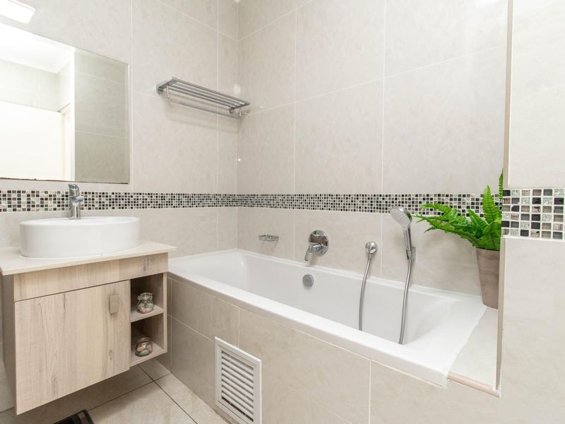 A modern bathroom featuring a built-in bathtub with a handheld showerhead, a vanity cabinet with a vessel sink, and neutral wall tiling.