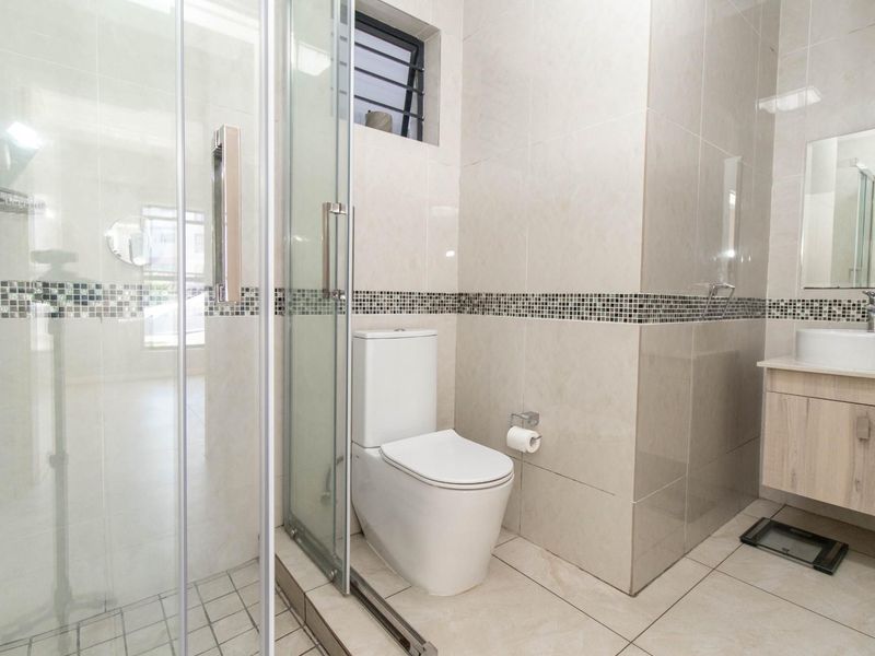 Modern bathroom featuring a glass-enclosed shower, wall-mounted vanity with basin, and tiled finishes throughout.