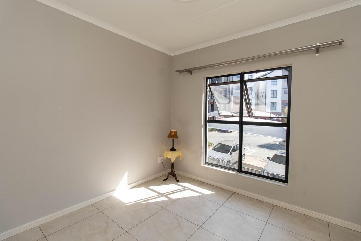 A bright, empty bedroom featuring neutral wall paint, tiled flooring, and a large window with a curtain rod.