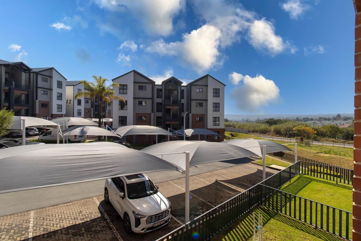 Exterior view of the apartment complex featuring paved parking areas with shade cloth carports and landscaped grounds.