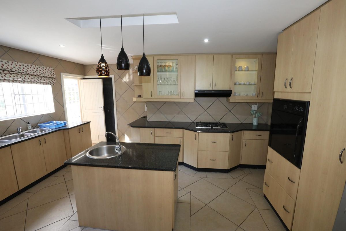 A functional kitchen featuring light wood cabinetry, dark granite countertops, a central island with a prep sink, and built-in oven and gas hob.