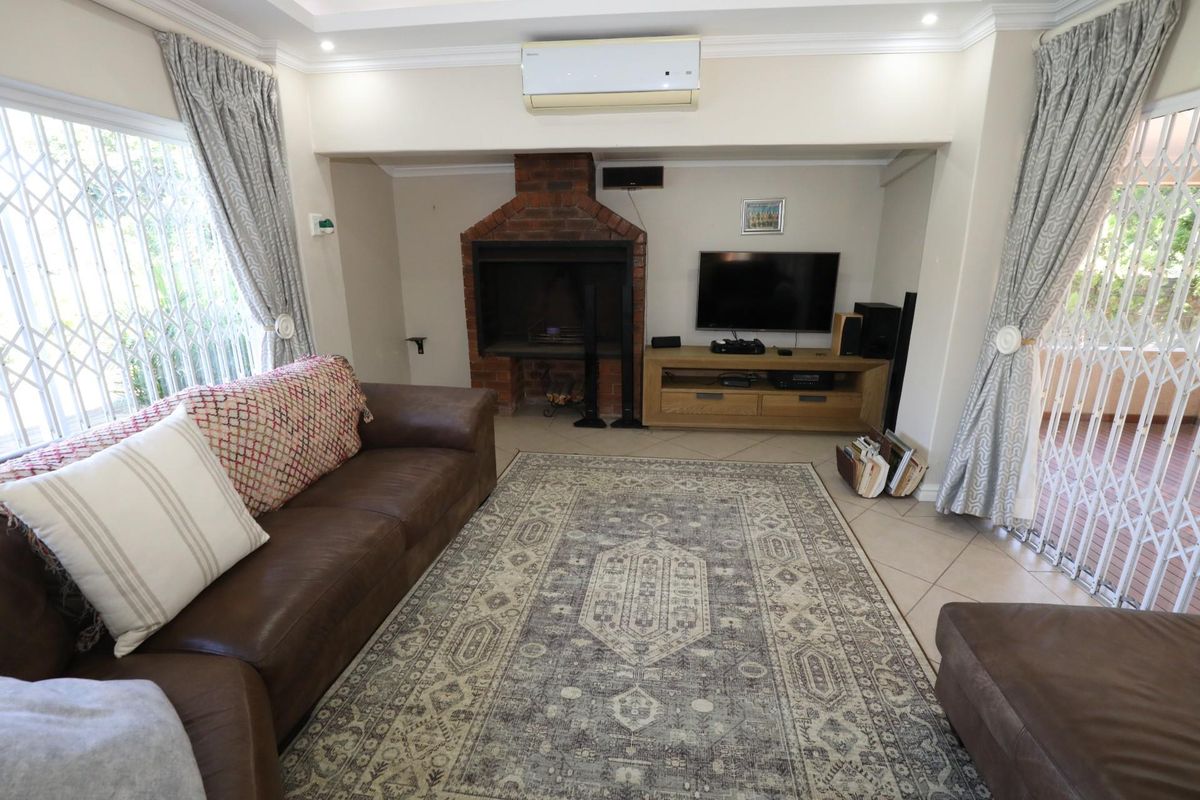 A comfortable living room featuring a built-in brick fireplace, tiled flooring, recessed ceiling lighting, and a wall-mounted air conditioning unit.