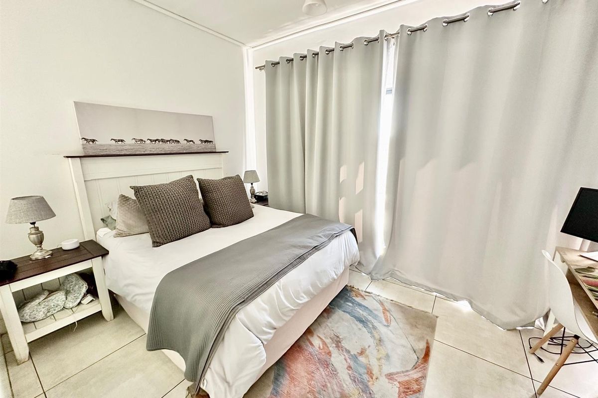 A bright and well-maintained bedroom featuring neutral tiled flooring and large window curtains, providing a clean and comfortable living space.