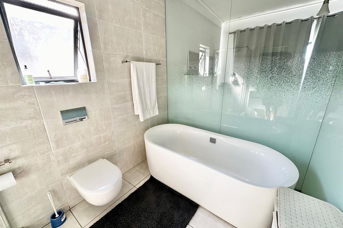 Modern bathroom featuring a sleek freestanding bathtub, wall-mounted toilet, and a glass shower screen with contemporary neutral tiling.