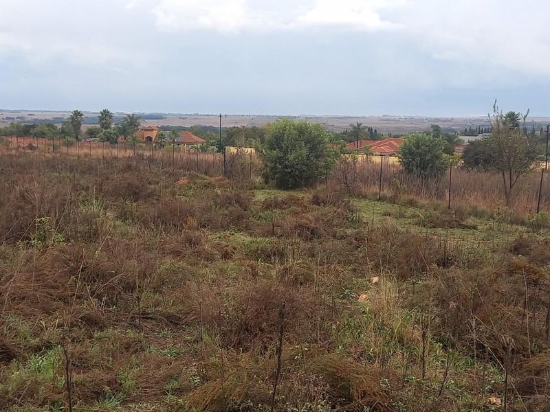 A vacant residential plot featuring natural vegetation, perimeter fencing, and expansive views of the surrounding landscape and neighborhood.
