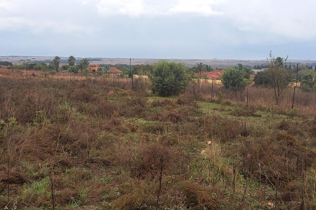 A vacant residential plot featuring natural vegetation, perimeter fencing, and expansive views of the surrounding landscape and neighborhood.