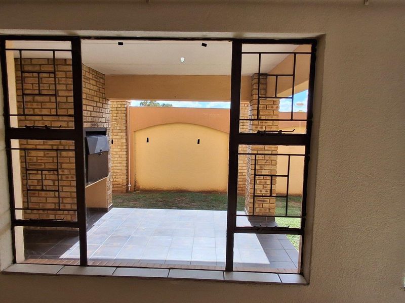 View from an interior room looking out onto a covered patio featuring a built-in braai and a private enclosed garden area.