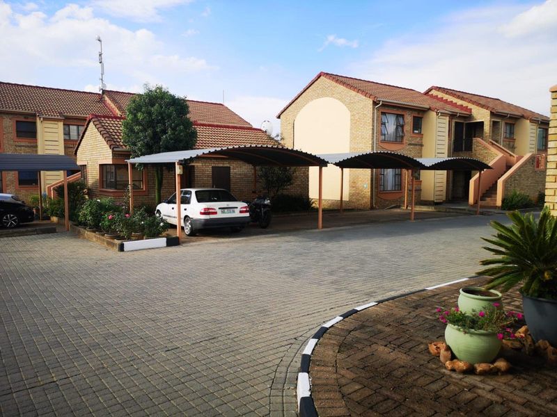 Exterior view of a townhouse complex featuring brick facades, tiled roofs, and covered parking bays with paved driveway access.