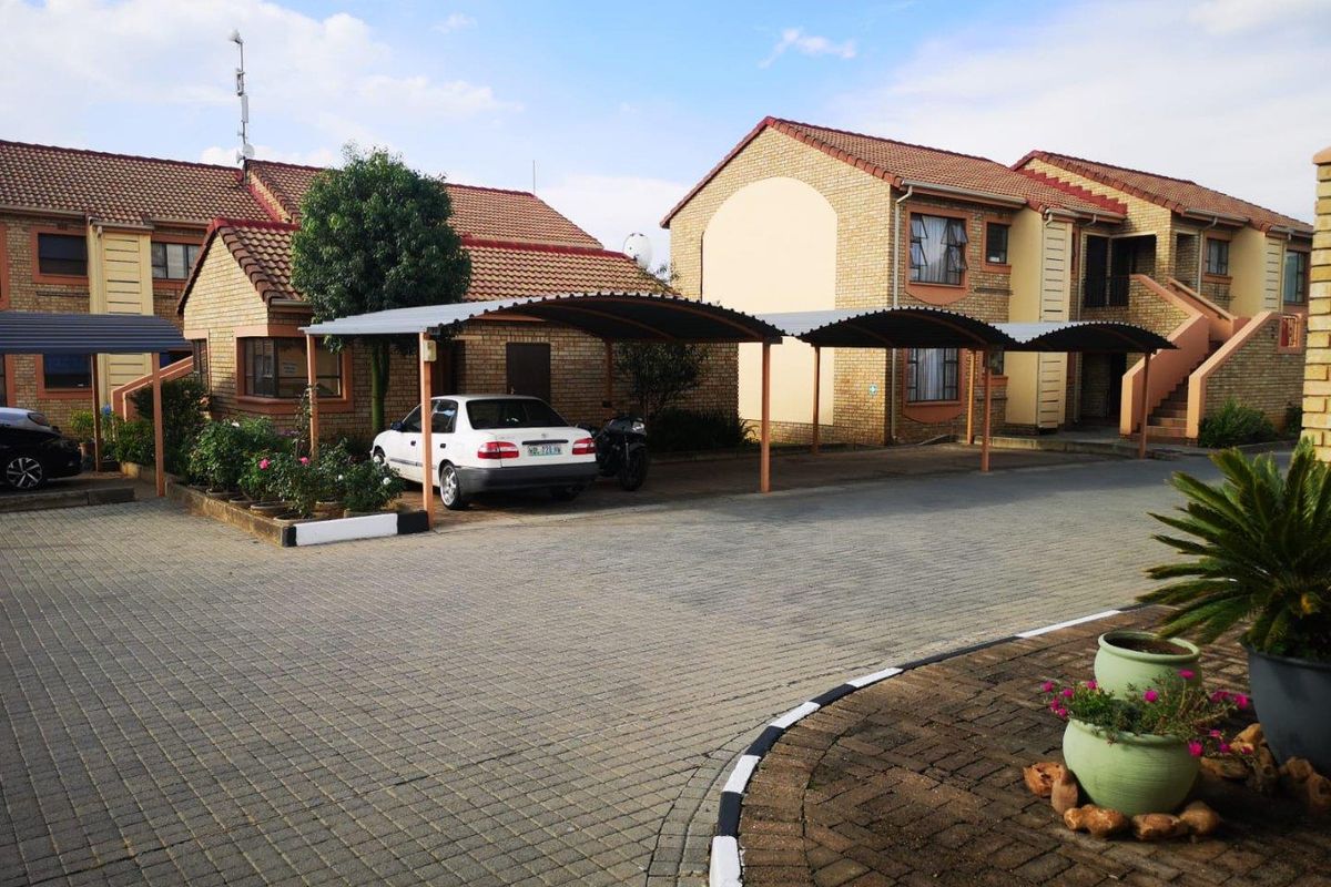 Exterior view of a townhouse complex featuring brick facades, tiled roofs, and covered parking bays with paved driveway access.
