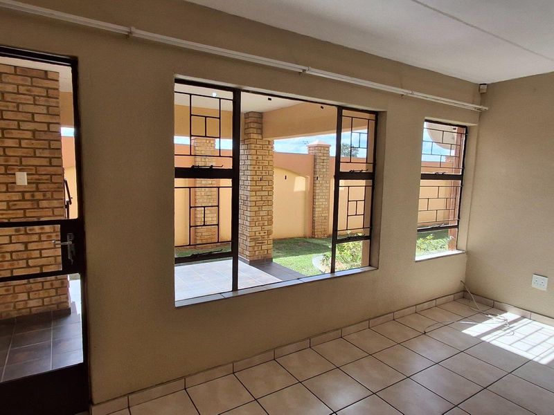 A bright, empty living area featuring large windows with security bars, tiled flooring, and direct access to an outdoor patio space.