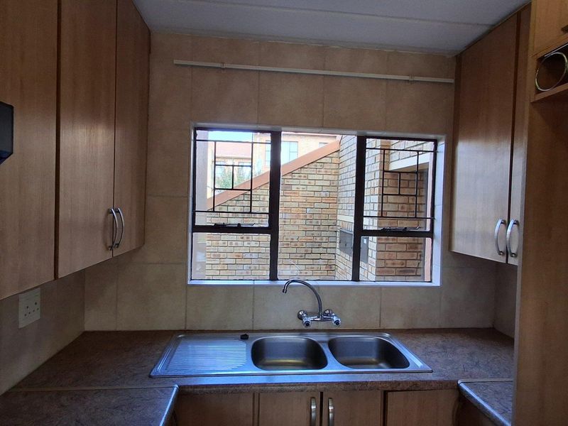 A functional kitchen area featuring wooden cabinetry, a double-basin stainless steel sink, and a window overlooking the exterior brickwork.