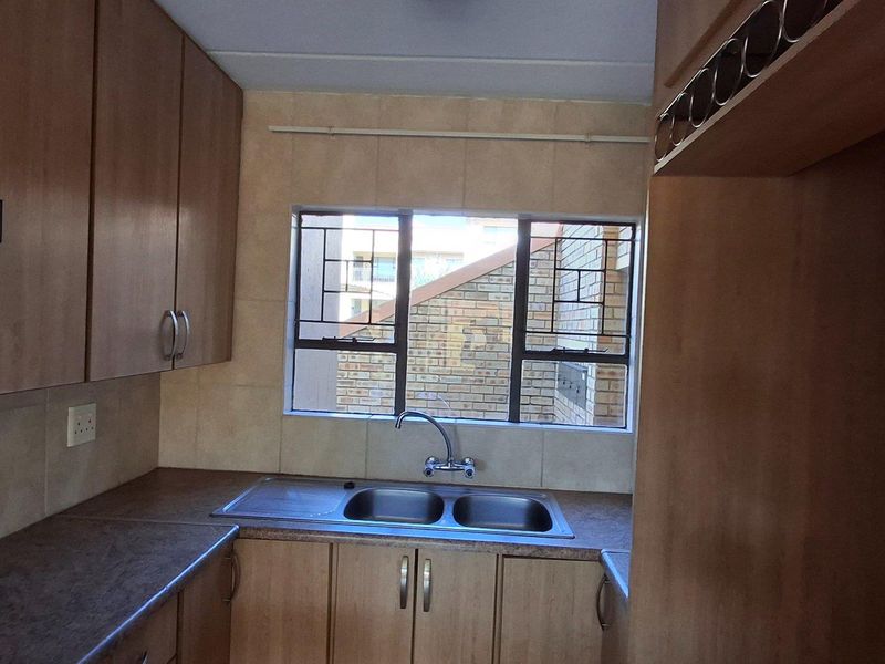 A functional kitchen featuring wooden cabinetry, a double stainless steel sink, tiled splashbacks, and a built-in extractor fan.
