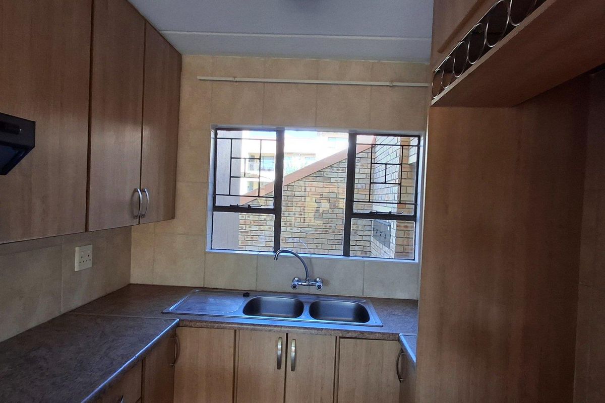 A functional kitchen featuring wooden cabinetry, a double stainless steel sink, tiled splashbacks, and a built-in extractor fan.