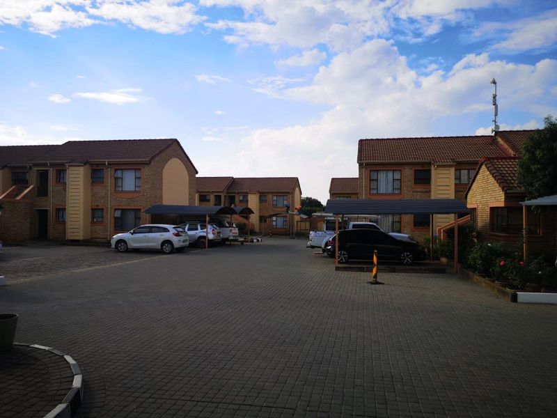 A view of the townhouse complex parking area featuring paved driveways, covered carports, and multi-story brick residential units.