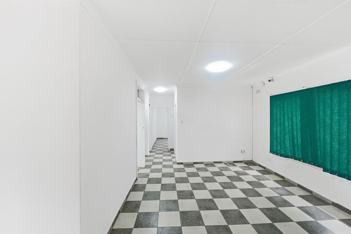 An empty living area featuring checkered tile flooring, white walls, and a hallway leading to additional rooms.