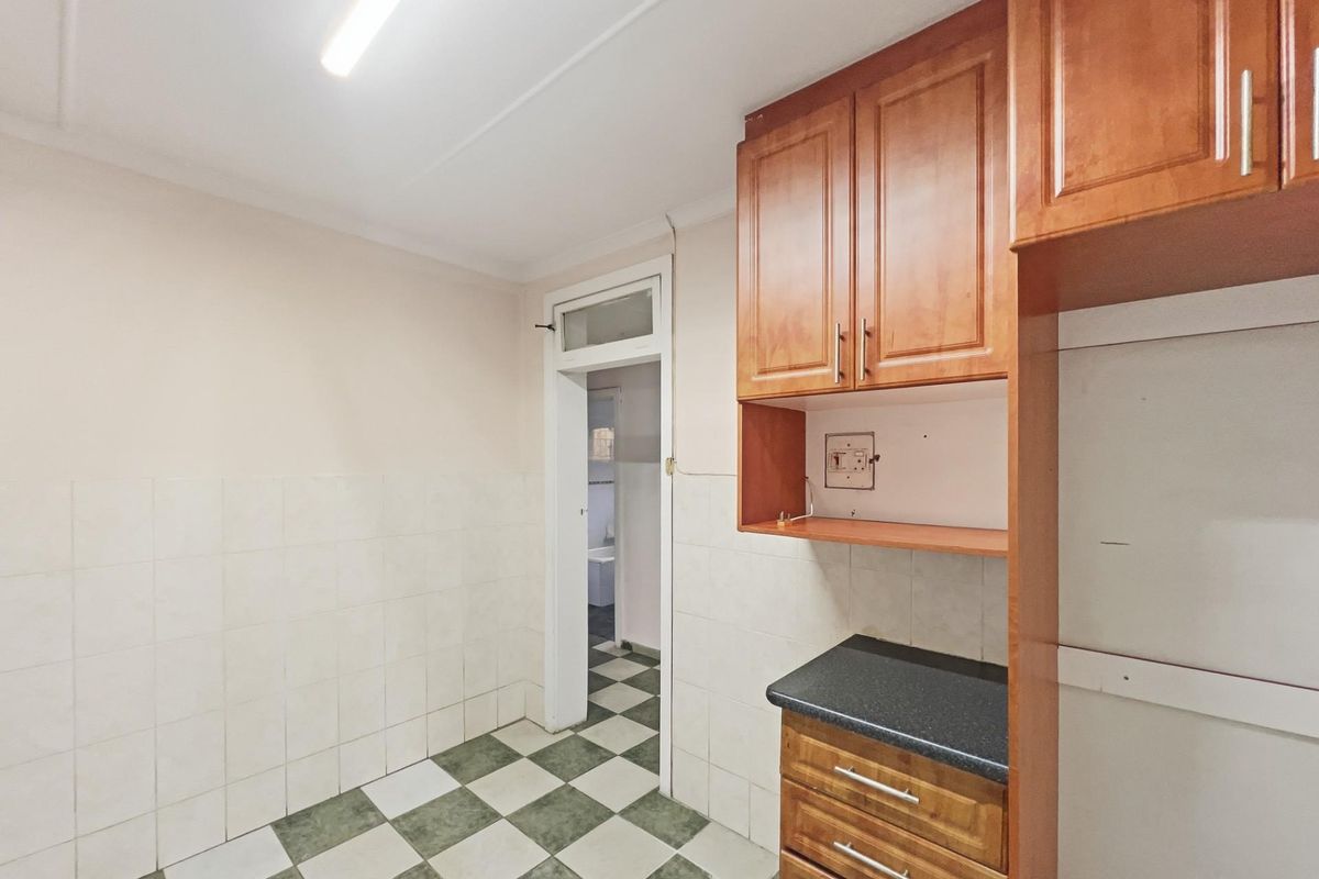 A functional kitchen area featuring wooden cabinetry, tiled splashbacks, and a checkered floor, providing a practical space for culinary preparation.