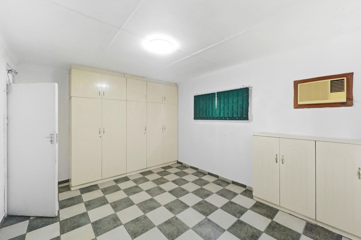 A functional bedroom featuring built-in floor-to-ceiling cabinetry, checkered floor tiling, and a wall-mounted air conditioning unit.