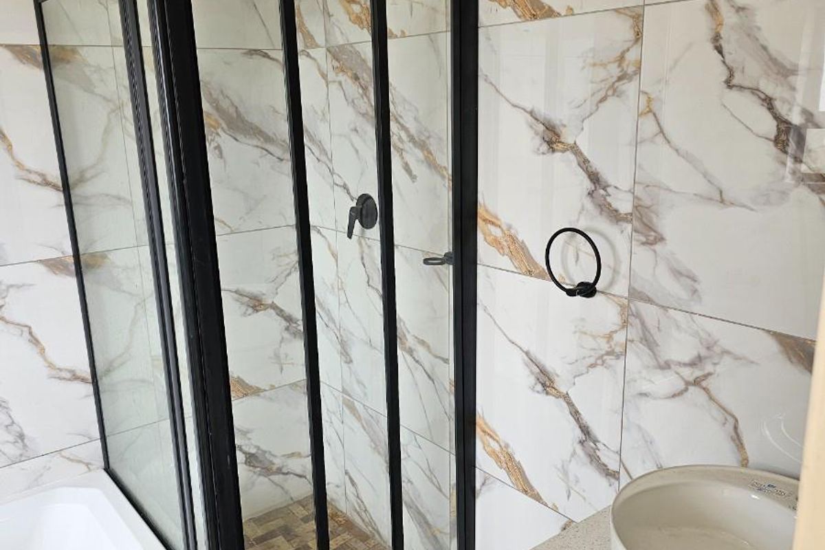 Modern bathroom featuring a glass-enclosed shower with black frame, marble-look wall tiles, and a contemporary vessel sink vanity.