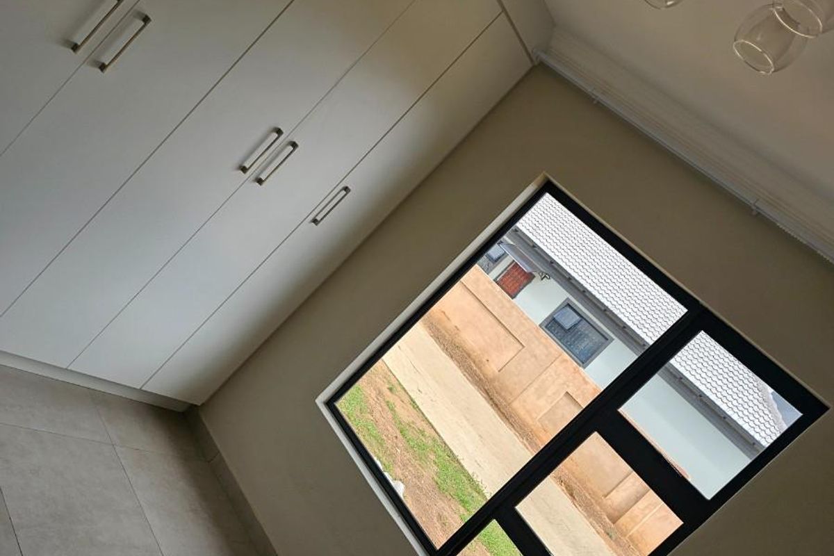 A bright bedroom featuring neutral floor tiles, built-in floor-to-ceiling wardrobes, and a large window providing natural light.