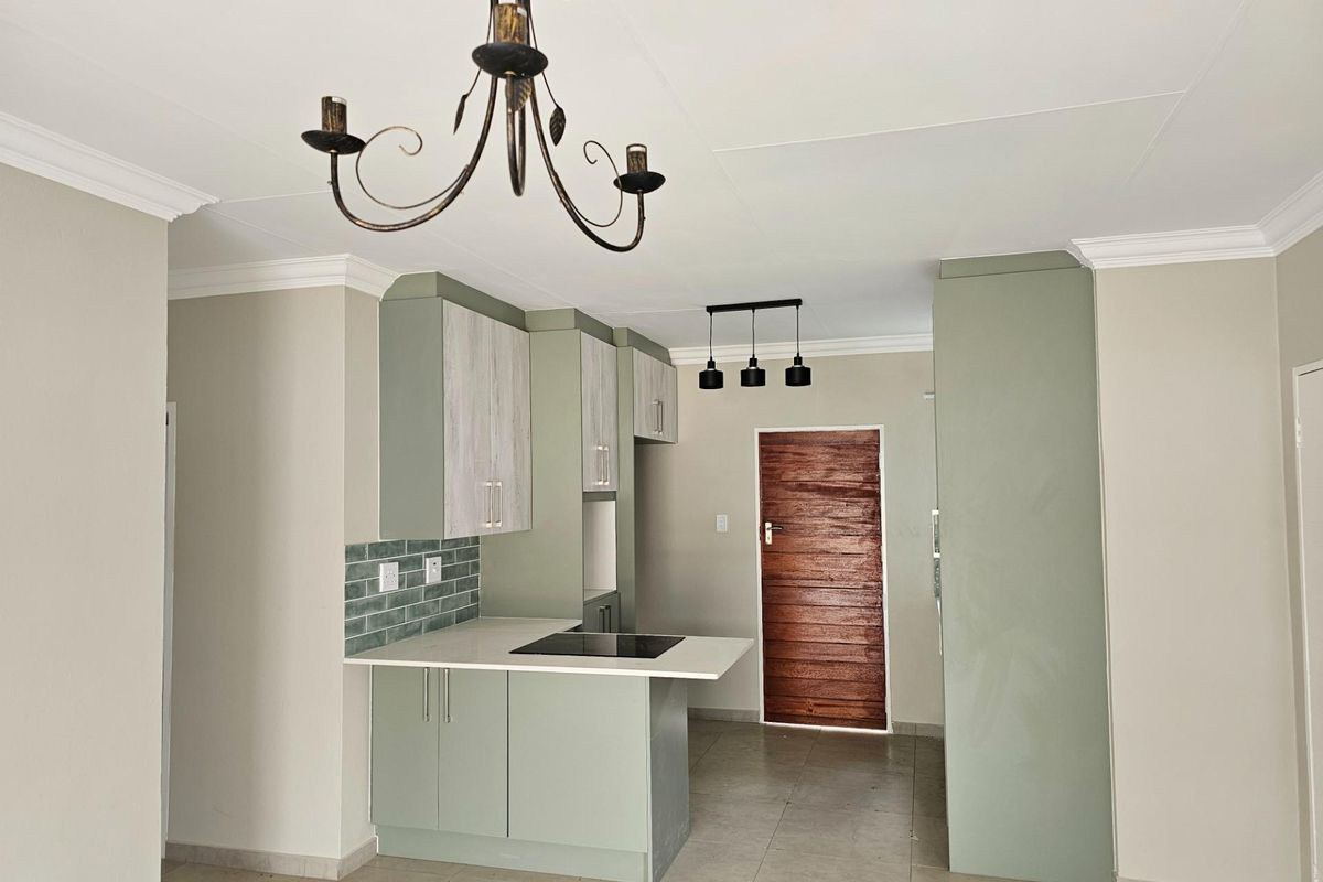 Modern kitchen featuring sage green cabinetry, stone countertops, a built-in electric hob, and tiled flooring, complemented by decorative pendant lighting.