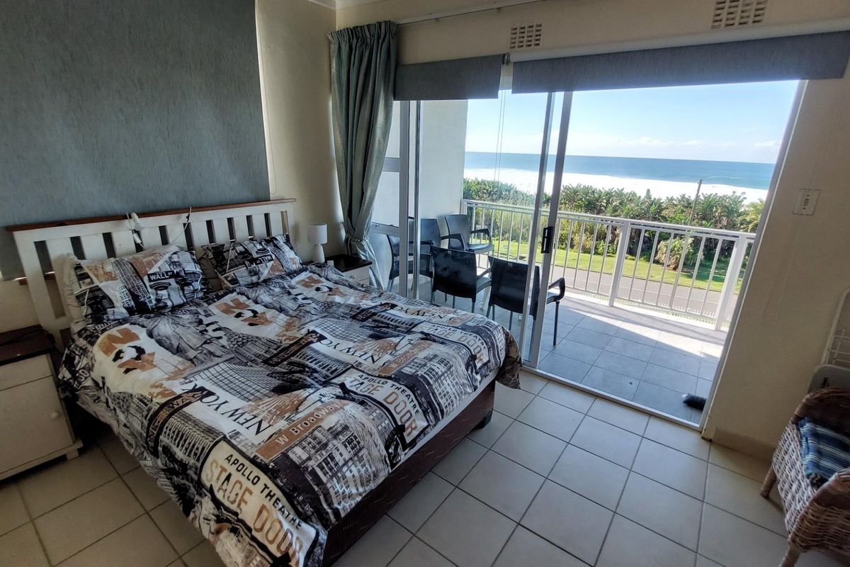 A bedroom featuring tiled flooring and large sliding glass doors that open onto a balcony with scenic ocean views.