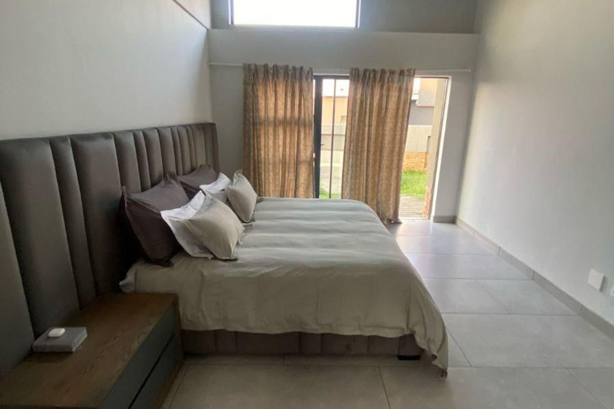 Spacious bedroom featuring high ceilings, large format floor tiles, and direct access to the garden through a sliding glass door.