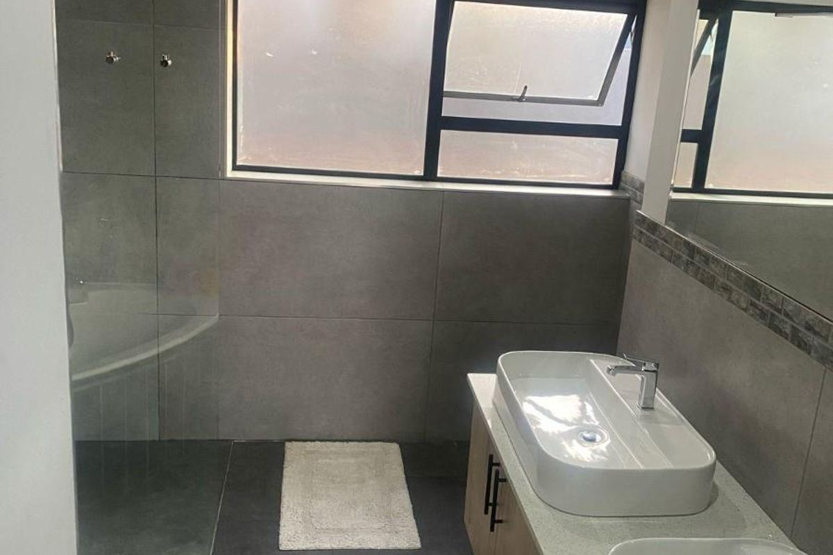 Modern bathroom featuring a double vanity with stone countertop, large grey floor-to-ceiling tiles, and a glass-enclosed shower area.