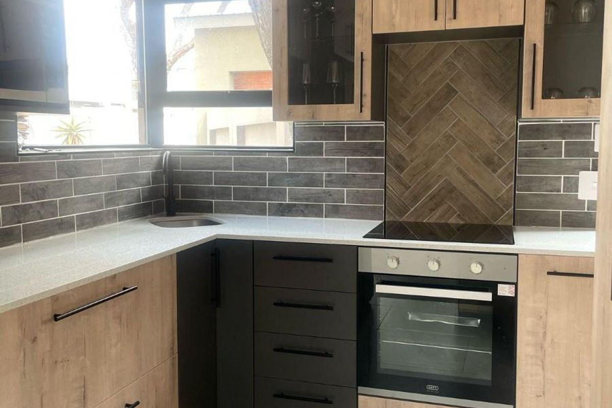Modern kitchen featuring wood-grain cabinetry, stone countertops, a built-in oven with hob, and stylish herringbone tile backsplash.
