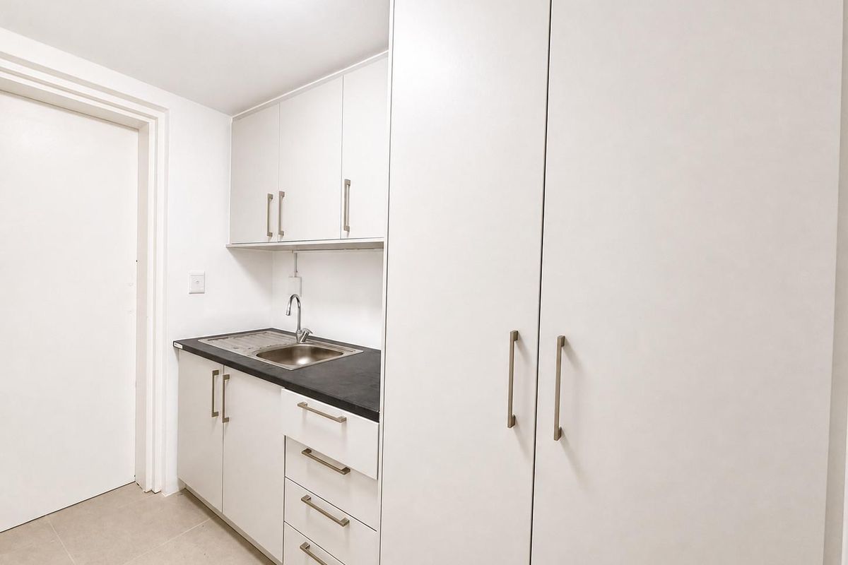 A clean and functional kitchenette featuring white cabinetry, a stainless steel sink, and ample storage space, suitable for office or utility use.