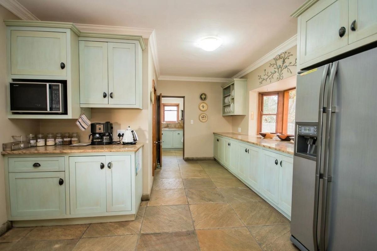 A spacious kitchen featuring light green cabinetry, stone-look tiled flooring, granite countertops, and a built-in microwave, with a view through to a secondary prep area.