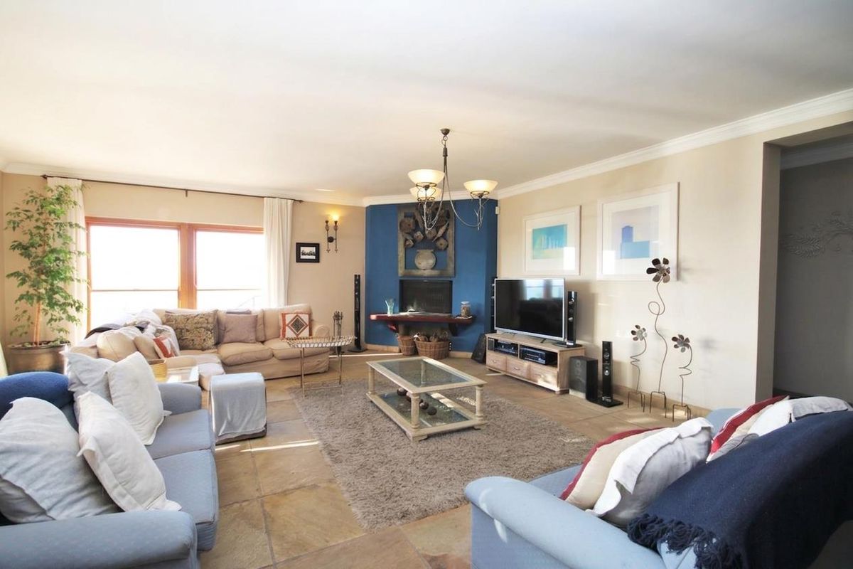 Spacious living room featuring tiled flooring, a central fireplace with a blue accent wall, and large windows providing natural light.