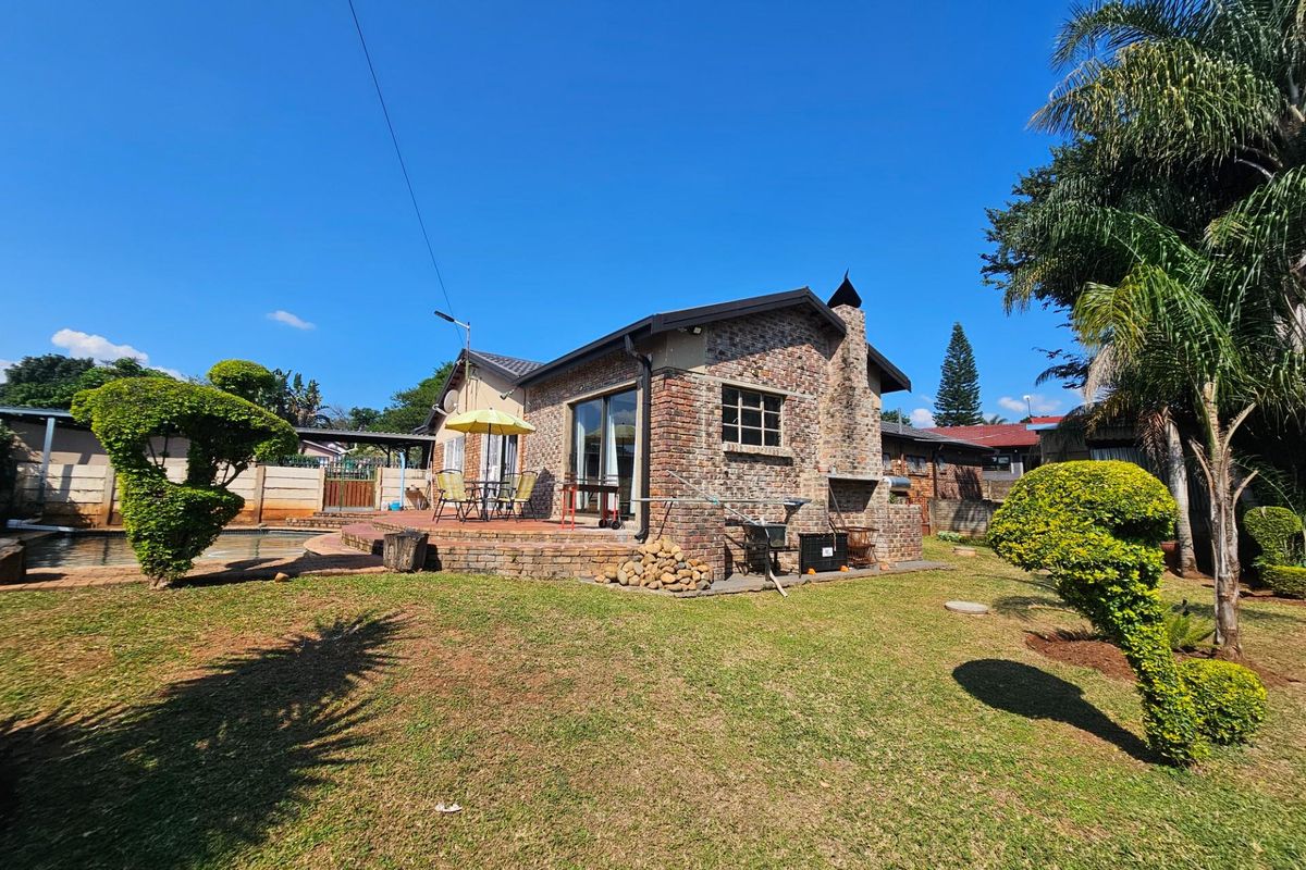Rear view of the house featuring a face-brick exterior, built-in outdoor fireplace, paved patio area, and a spacious garden with established landscaping.