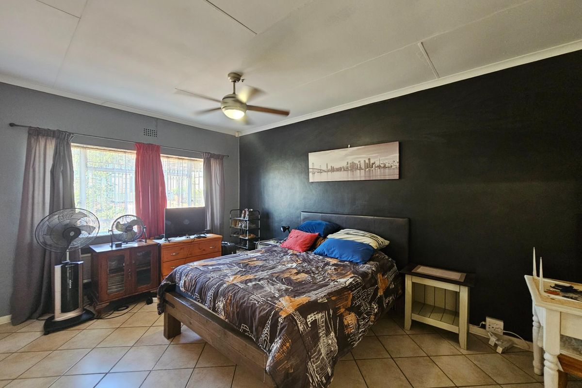 A bedroom featuring tiled flooring, a ceiling fan, and a large window with security bars.