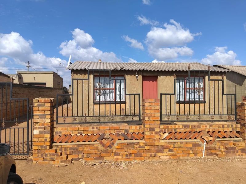 Front view of a single-story house featuring a brick boundary wall, metal security gates, and security bars on windows.