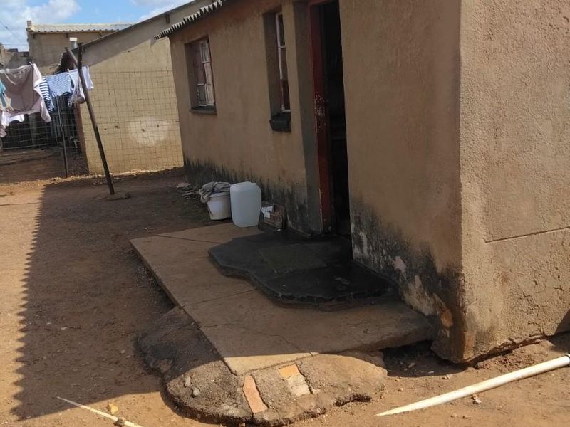 Exterior view of a small residential structure showing significant wear to the exterior plaster, foundation, and entrance area.
