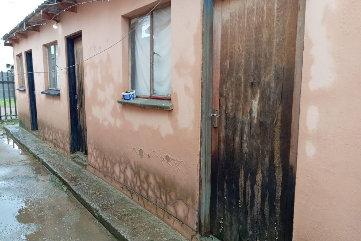 Exterior view of a residential building showing multiple entry points, weathered wooden doors, and visible signs of damp and plaster deterioration on the walls.