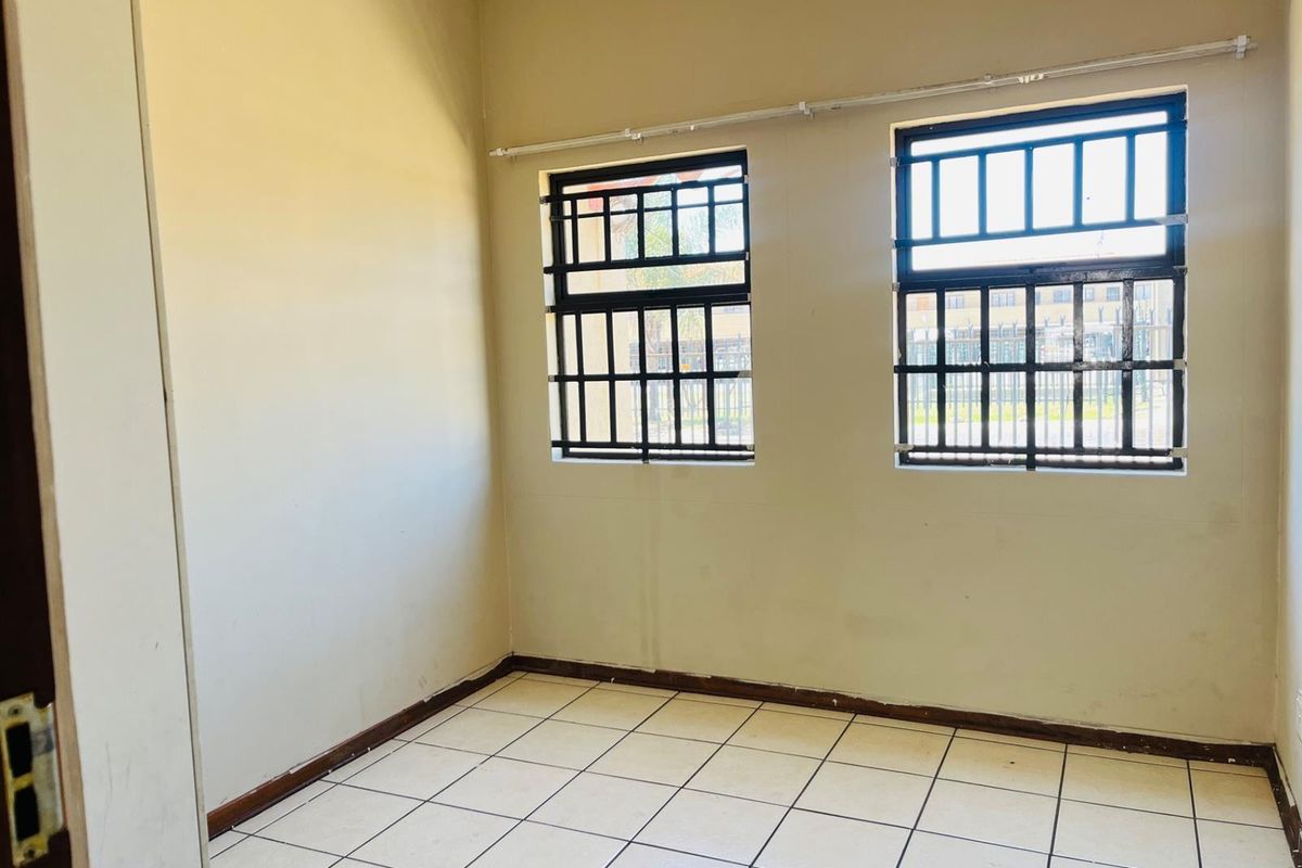 A vacant bedroom featuring tiled flooring and windows fitted with security burglar bars.
