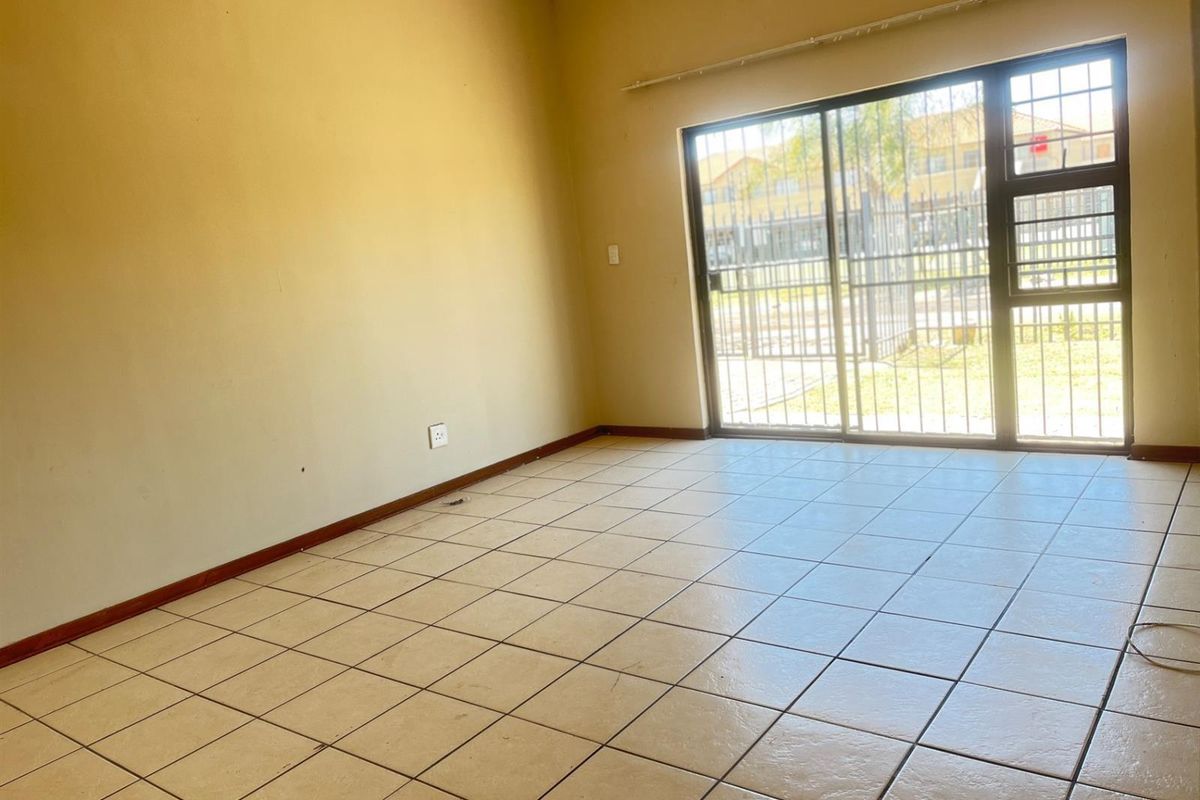 An empty living room featuring tiled flooring and a large sliding glass door with security bars, providing access to the exterior.