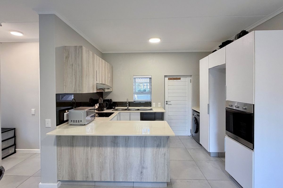 Modern kitchen featuring light wood-grain cabinetry, stone countertops, built-in oven, extractor fan, and integrated laundry space with tiled flooring.