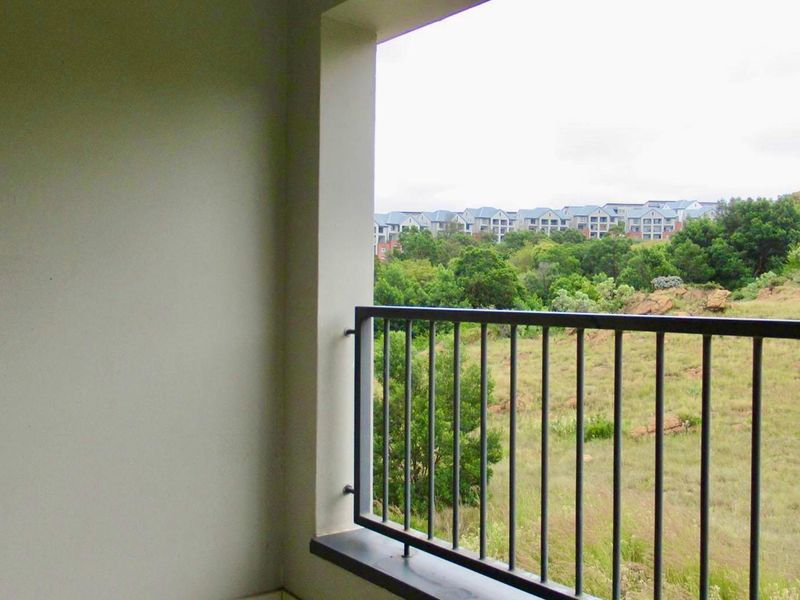 A covered balcony featuring a metal railing, offering scenic views of the surrounding landscape and neighboring residential complex.