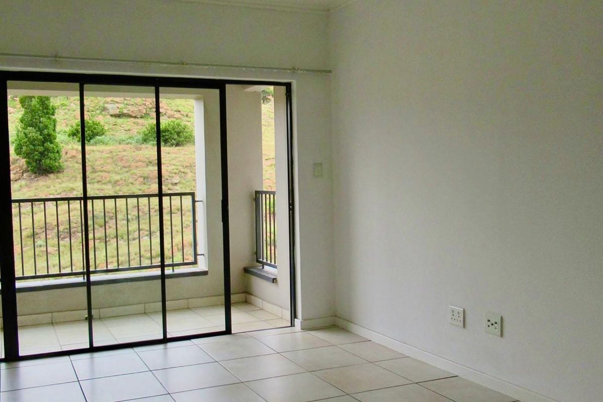 An empty living room featuring tiled flooring and large sliding glass doors that open onto a private balcony with scenic hillside views.