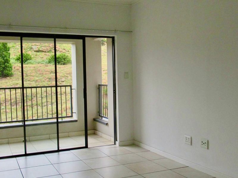 An empty living room featuring tiled flooring and large sliding glass doors that open onto a private balcony with scenic hillside views.