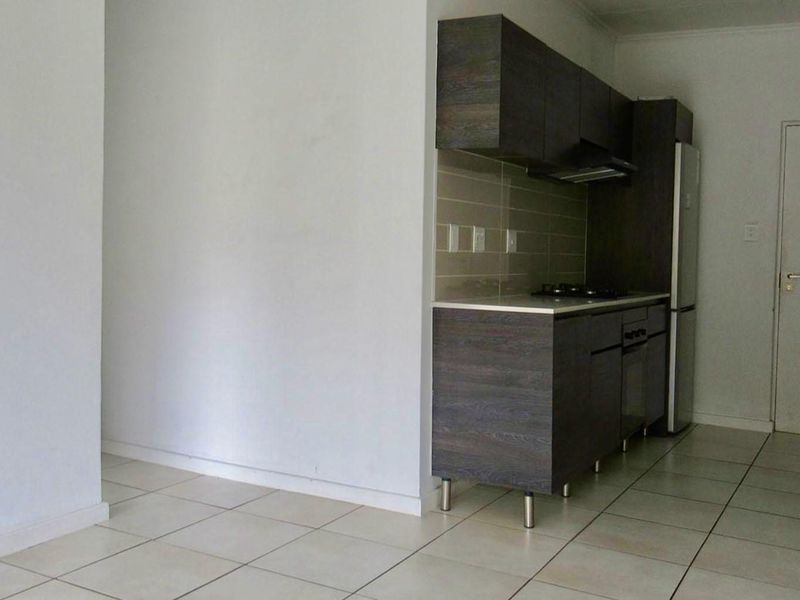 Compact kitchen featuring dark wood-look cabinetry, tiled flooring, built-in hob, and extractor fan, integrated into an open-plan living space.