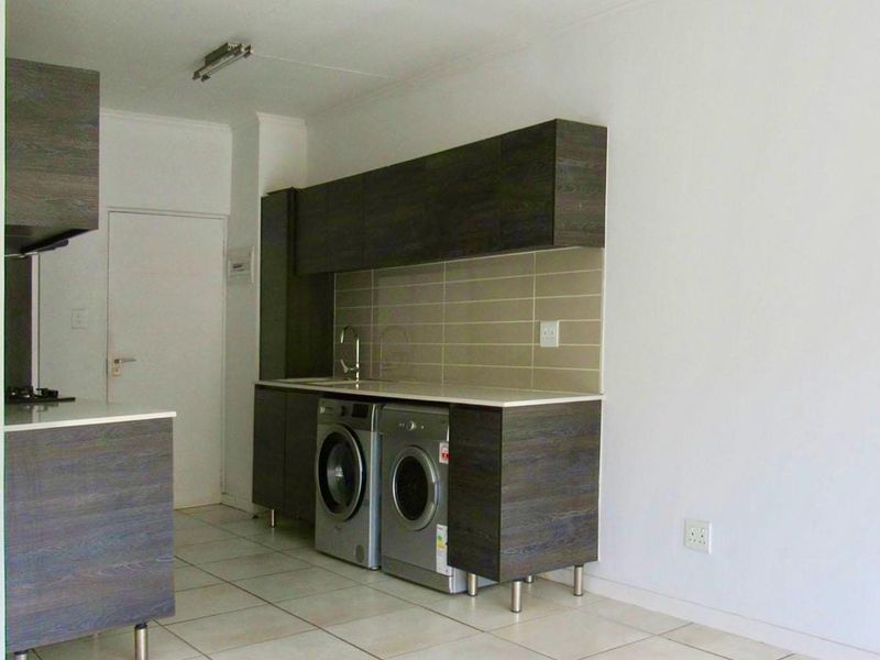 Modern kitchen featuring dark wood-grain cabinetry, light stone countertops, tiled backsplash, and integrated space for laundry appliances.